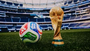 Soccer ball and the FIFA World Cup trophy resting on a grass field inside a large empty stadium.