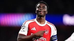Arsenal footballer in red jersey with white sleeves, wearing a captain's armband on the pitch during a match.