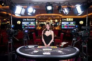 Hostess in a black dress stands at a casino baccarat table, surrounded by cameras and bright studio lights in a live‑casino setup.