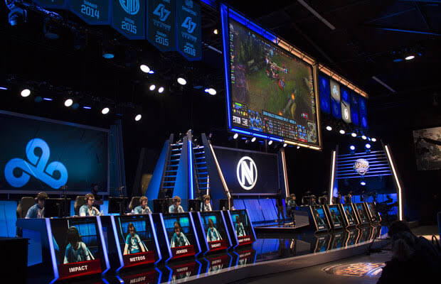 - 香港Gameone娛樂城全新會員福利 - 入金00即返送00! Esports tournament stage with players at neon-lit desks and a large screen showing gameplay.