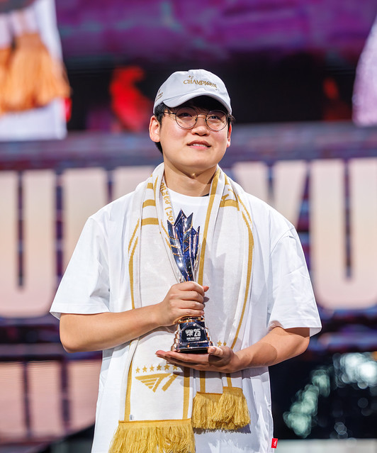 - 香港Gameone娛樂城全新會員福利 - 入金00即返送00! Person on stage wearing a white shirt and cap, holding a tall trophy with a gold scarf draped over the shoulders, smiling at the camera.