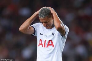 Footballer in a white Tottenham kit with AIA sponsor holding his head in frustration on the pitch.